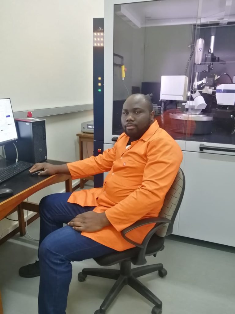 Dr Sodeeq Aderotimi sitting at a desk in front of a lab instrument