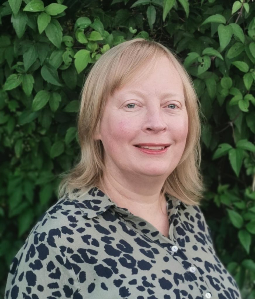 Photo of Sally Gaw in front of a green leafy hedge